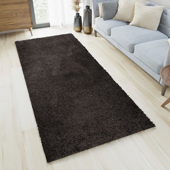 Un tapis shaggy gris foncé à poils longs dans un salon, à côté d'un canapé gris.