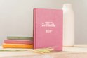 Roze dagboek 'Dagboek voor Zelfliefde' met stapeltje gekleurde dagboeken ernaast.