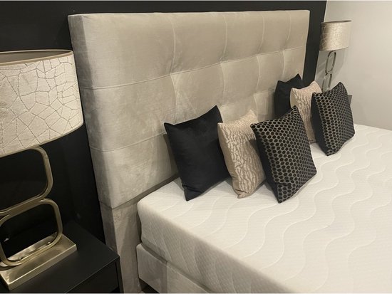 Gedetailleerd beeld van een beige boxspring met gestoffeerd hoofdbord, vier sierkussens en een lamp.