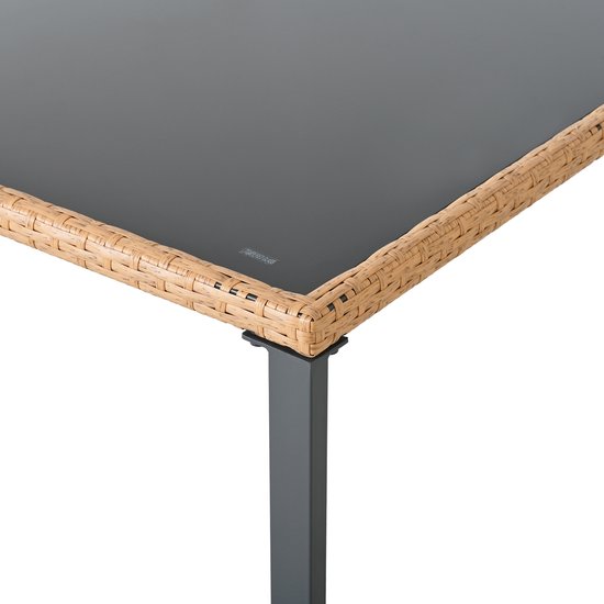 Detail van de hoek van een tafel met een bruine rotan rand en een zwart glazen tafelblad.