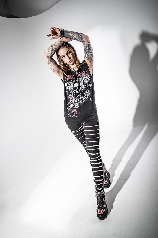 Model draagt een zwarte tanktop met een doodshoofd en vleugels opdruk en een broek met witte banden.