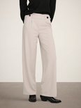 Lichtbeige wijde broek met plooitjes en zwarte knopen aan de voorkant, gedragen door een model.