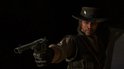 Close-up van een man met cowboyhoed, die een revolver vasthoudt, met een donkere achtergrond.