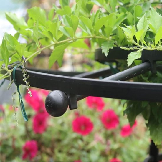 Zwarte plantenstandaard met groene bladeren en roze bloemen op de achtergrond.