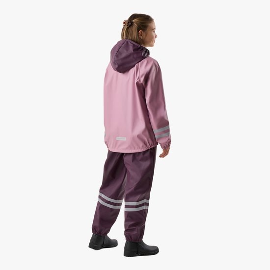 Meisje met lang bruin haar, van achteren gezien, in een roze regenjas met paarse capuchon en bretelbroek.