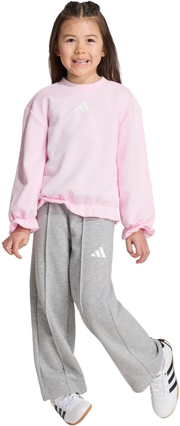 Meisje in roze sweater met ruches en grijze joggingbroek met Adidas-logo.