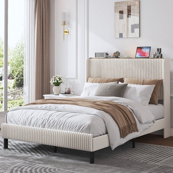 Lit rembourré beige côtelé, draps blancs, couverture marron, avec une œuvre d'art et une applique murale dorée.