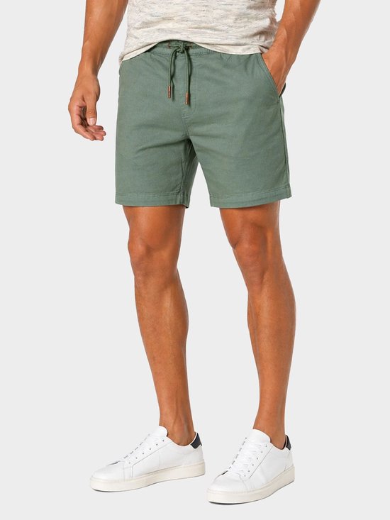 Man met groene chino shorts met trekkoord, T-shirt en witte sneakers.