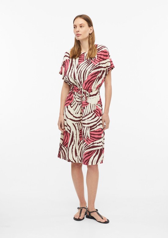 Model draagt een off-white T-shirtjurk met bruine en roze abstracte print, wijde mouwen en ceintuur in de taille.