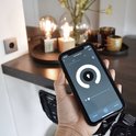 Hand houdt smartphone met lichtinstellingen, met gedimde lampen op achtergrond.