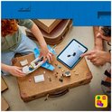 Jongen bouwt met tablet een wit en blauw LEGO vliegtuig op een bruine koffer.