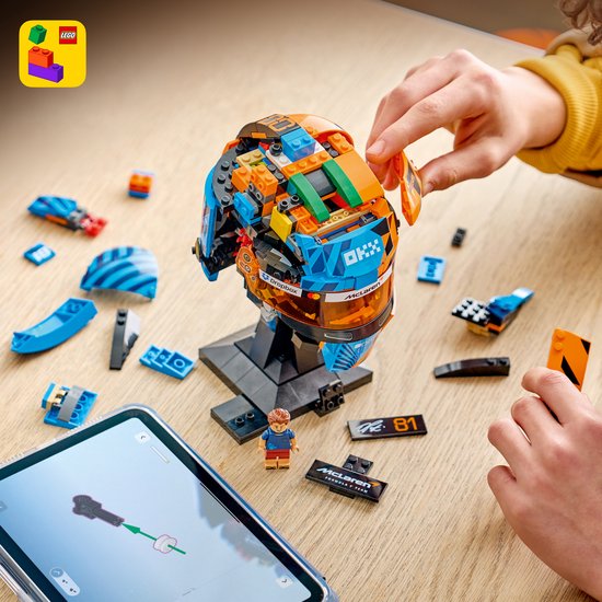 Kind bouwt LEGO McLaren F1 helm, blauw en oranje, met losse onderdelen en tablet.