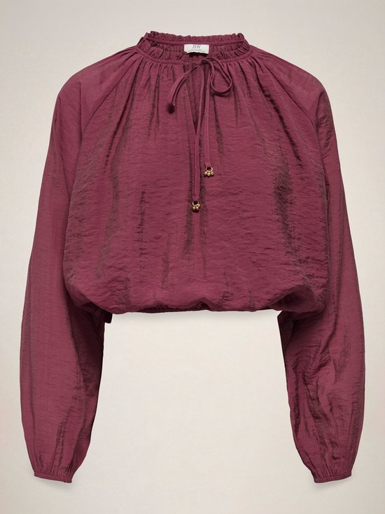 Bordeauxrode blouse met ruches, strikdetail en gouden knoopjes aan de zoom.