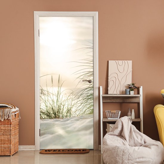 Deurposter met zandduinen en grassprieten bij zonsondergang, in een kamer met bruine muren en een welkomstmat.