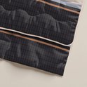 Detail van een dekbed met donkergrijs ruitpatroon en beige biezen.