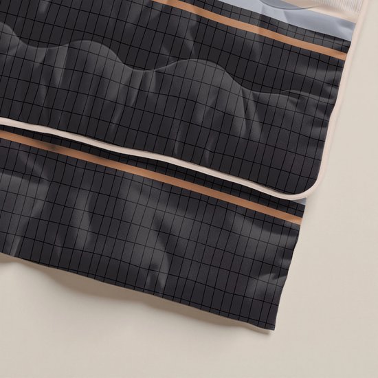 Detail van een dekbed met donkergrijs ruitpatroon en beige biezen.