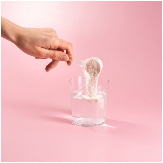 Hand schept wit collageenpoeder met een schepje in een glas water op een roze achtergrond.