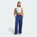 Model in een donkerblauwe trainingsbroek met witte strepen, Adidas logo en witte sneakers, staand met handen in de zakken.