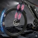 Voorwiel van een zwarte elektrische mountainbike met rode gloeiende schokdempers en blauwe energiestromen.
