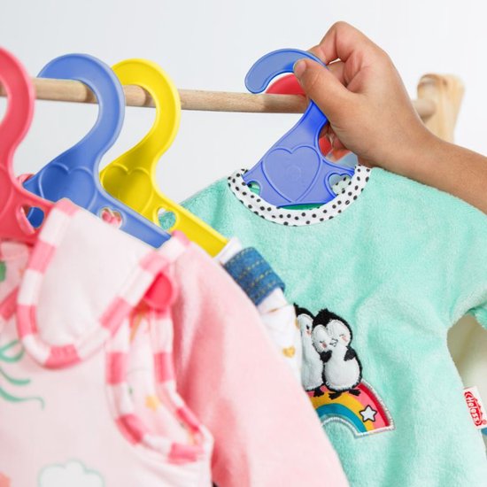 Een kind pakt een mintgroene poppenjurk met pinguïns op een regenboog van een gele kledinghanger.