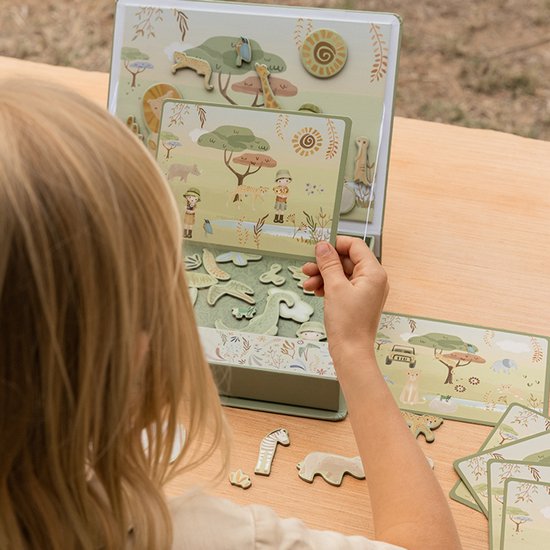 Meisje houdt een magnetische speelkaart met safari dieren vast boven een open speelbord.