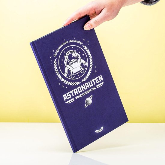 Een paars vriendenboek met een zilveren afbeelding van een astronaut in een cirkel van lauriertakken, vastgehouden door een hand.