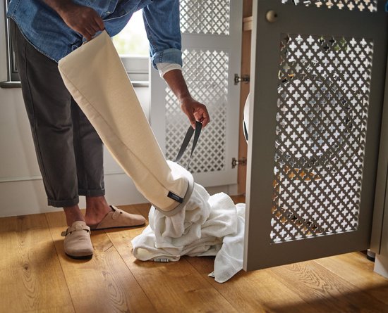 Witte handdoeken uit de ecru wasmand gehaald, op een houten vloer.