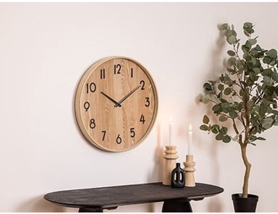Houten wandklok met zwarte cijfers en wijzers, aan een witte muur.