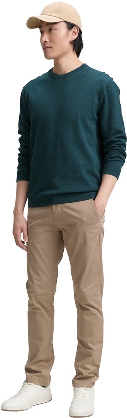Man in donkergroene trui, beige chino en pet.
