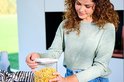 Une femme aux cheveux bruns bouclés ferme une boîte de conservation transparente remplie de pâtes farfalle.