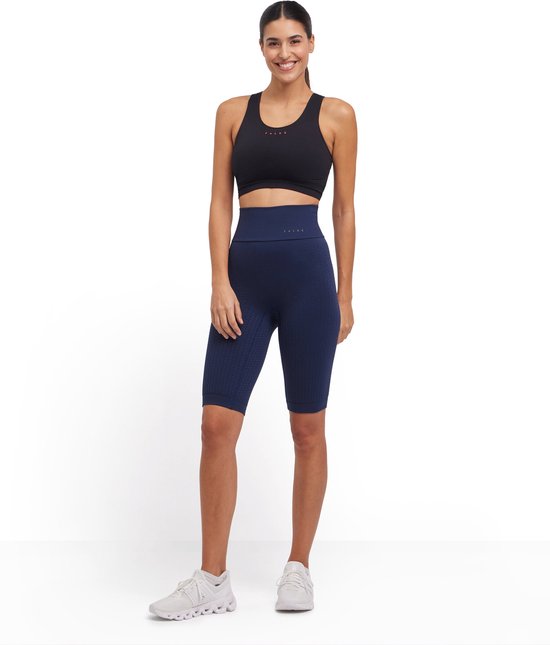 Model in een marineblauwe, hoge taille, nauwsluitende fietsbroek met een subtiel structuurpatroon en een zwarte sportbeha.