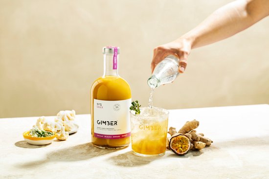 GIMBER LILLY wordt in een glas met ijs gemengd met bruisend water. Ernaast liggen gember en passievrucht.