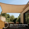Beige rechthoekig schaduwdoek hangend boven een terras met houten tafel en stoelen. Textuur van het materiaal is zichtbaar.