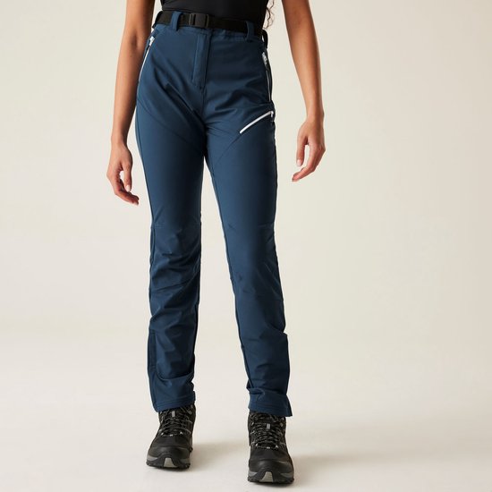 Model staat in een donkerblauwe outdoorbroek met witte accenten op de ritsen.