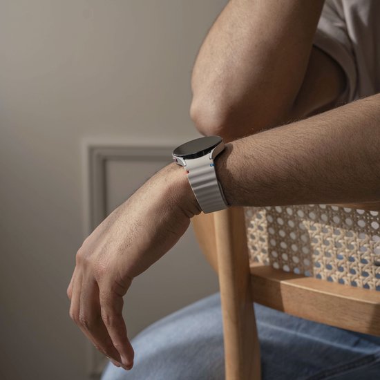 Mannelijk pols met een smartwatch en een crèmekleurig siliconen horlogebandje met golvend patroon, zittend.