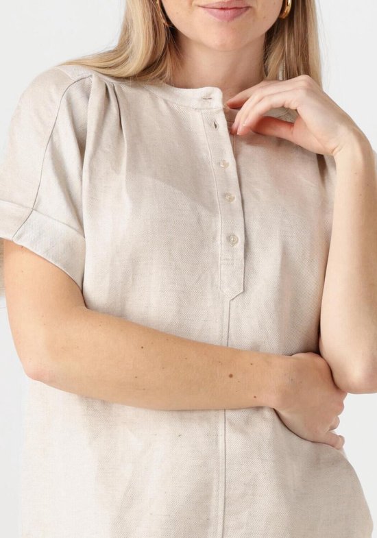 Close-up van de beige linnen blouse met knoopjes en gerimpelde schouders.