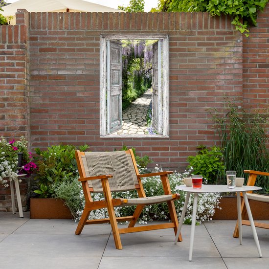 Een tuinposter met een doorkijk door een open deur naar een bloeiend pad, geplaatst tegen een bakstenen muur met tuinmeubilair.
