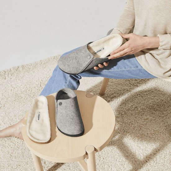 Vrouw toont grijze Birkenstock pantoffels met schapenwollen voering en een losse binnenzool.