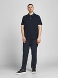 Man in donkerblauw poloshirt, donkere jeans en zwarte sneakers.