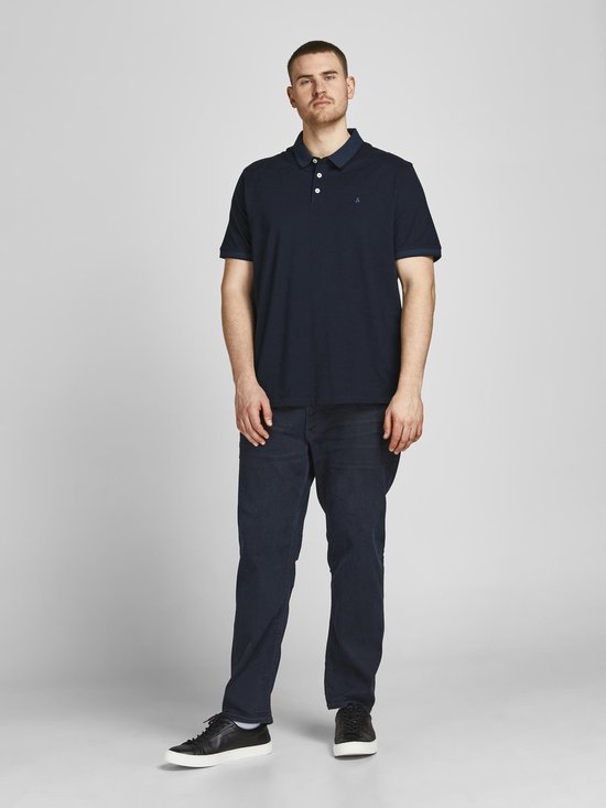 Man in donkerblauw poloshirt, donkere jeans en zwarte sneakers.