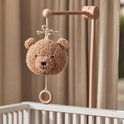 Lichtbruine teddybeer-muziekhanger met houten ring boven een kinderbedje.