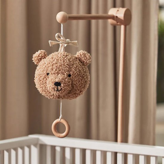 Lichtbruine teddybeer-muziekhanger met houten ring boven een kinderbedje.