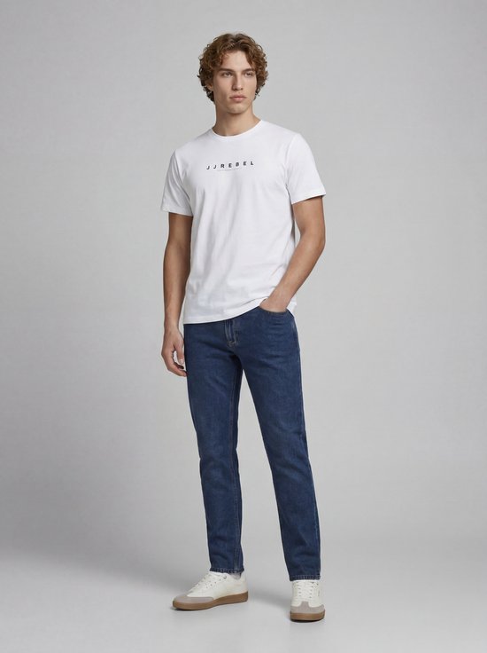 Jonge man in witte T-shirt met 'JJ REBEL' opdruk en donkerblauwe jeans.