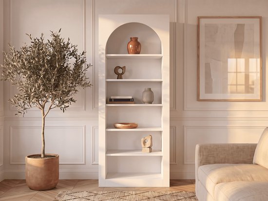 Witte CYMORA boekenkast met 6 nissen en boogvormige bovenkant, gevuld met decoratieve vazen en objecten.