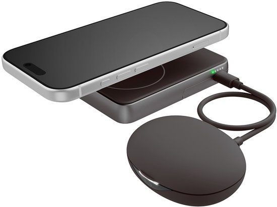 Donkergrijze magnetische powerbank verbonden met een oplaadpad, naast een smartphone in een witte behuizing.