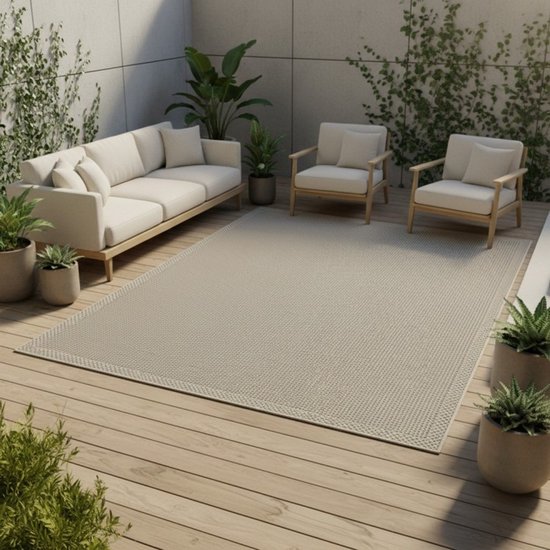 Tapis tissé à plat gris beige avec bordure, disposé sur une terrasse moderne avec canapé et fauteuils.