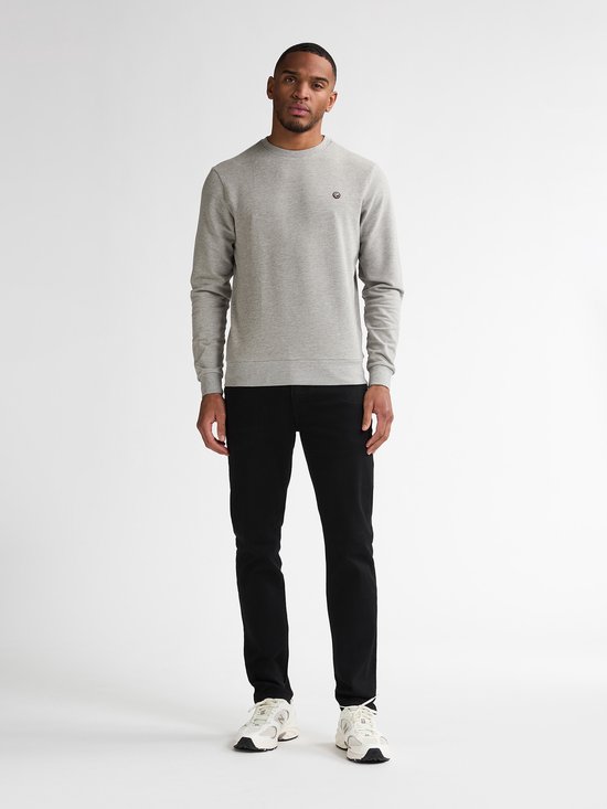 Model draagt een grijze trui en een zwarte slim fit jeans met witte sneakers.