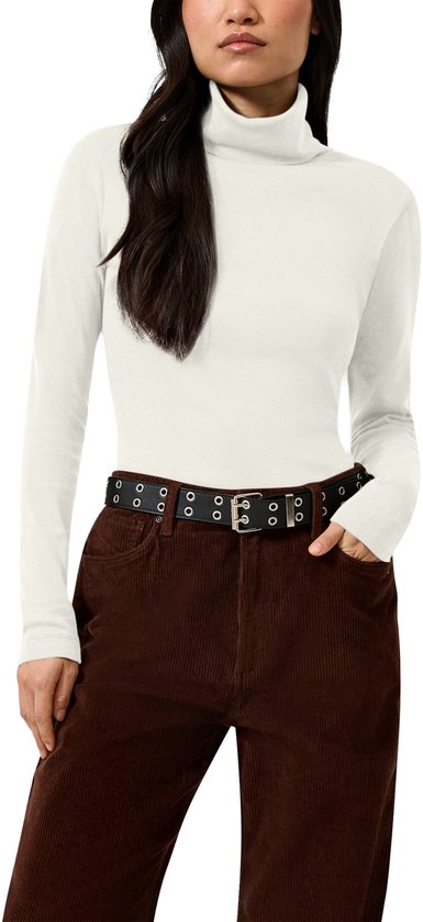 Model draagt een witte coltrui met lange mouwen en een zwarte riem met zilveren oogjes op bruine ribfluwelen broek.