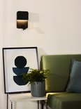 Zwarte wandlamp met verstelbare spot verlicht een slaapkamer met modern kunstwerk en groene bank.
