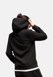 Zwarte Puma hoodie, gezien vanaf de achterkant terwijl een model de capuchon over het hoofd trekt.
